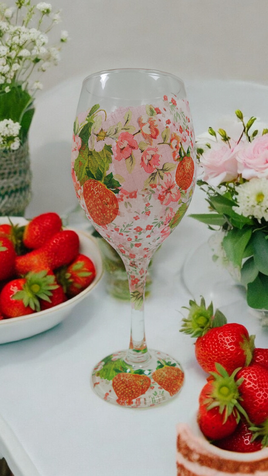 Decorative Decoupage wine glass with strawberry and floral pattern on a table with strawberries and flowers.