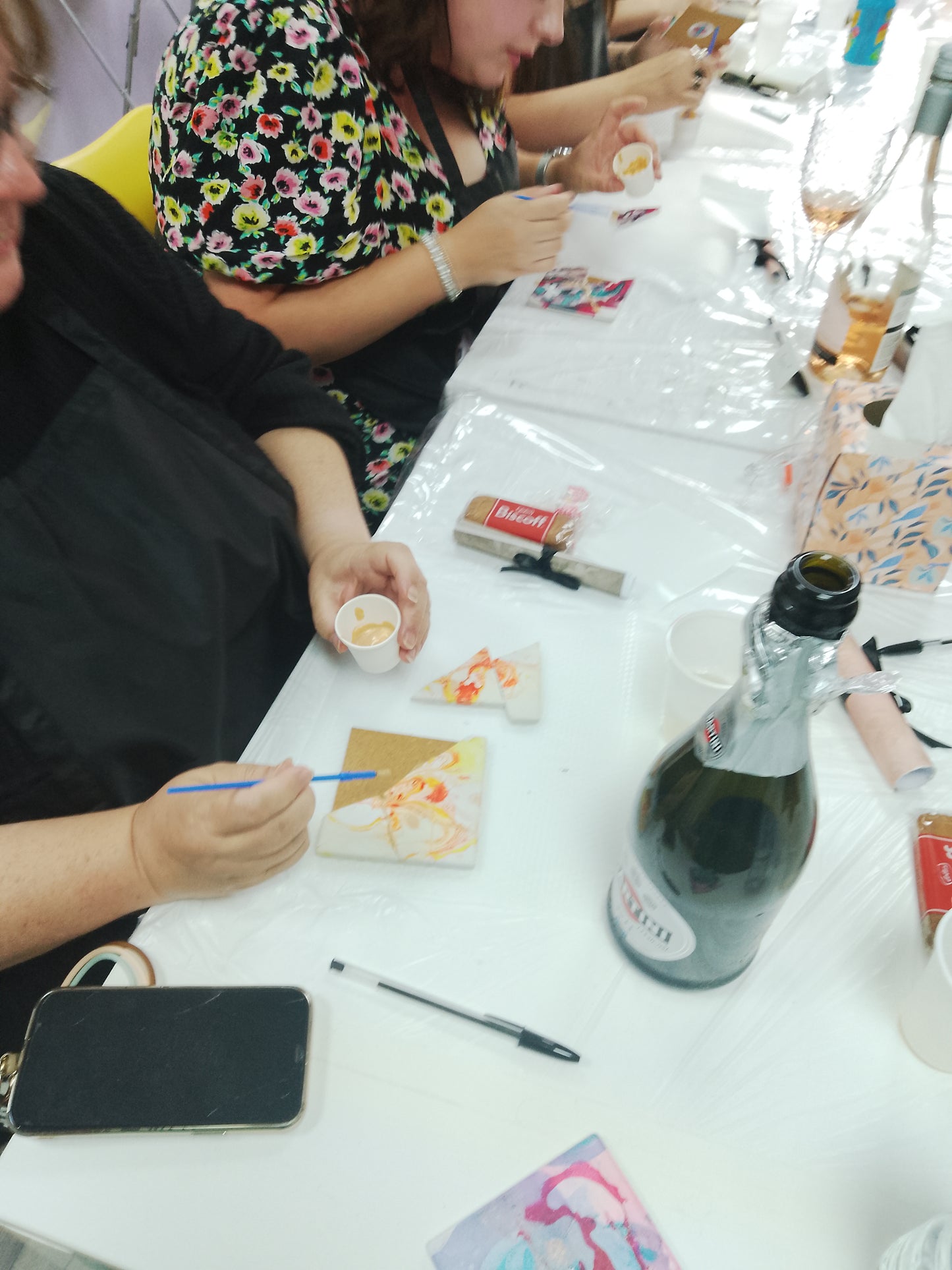 People sitting at a table with art supplies and a bottle of wine.