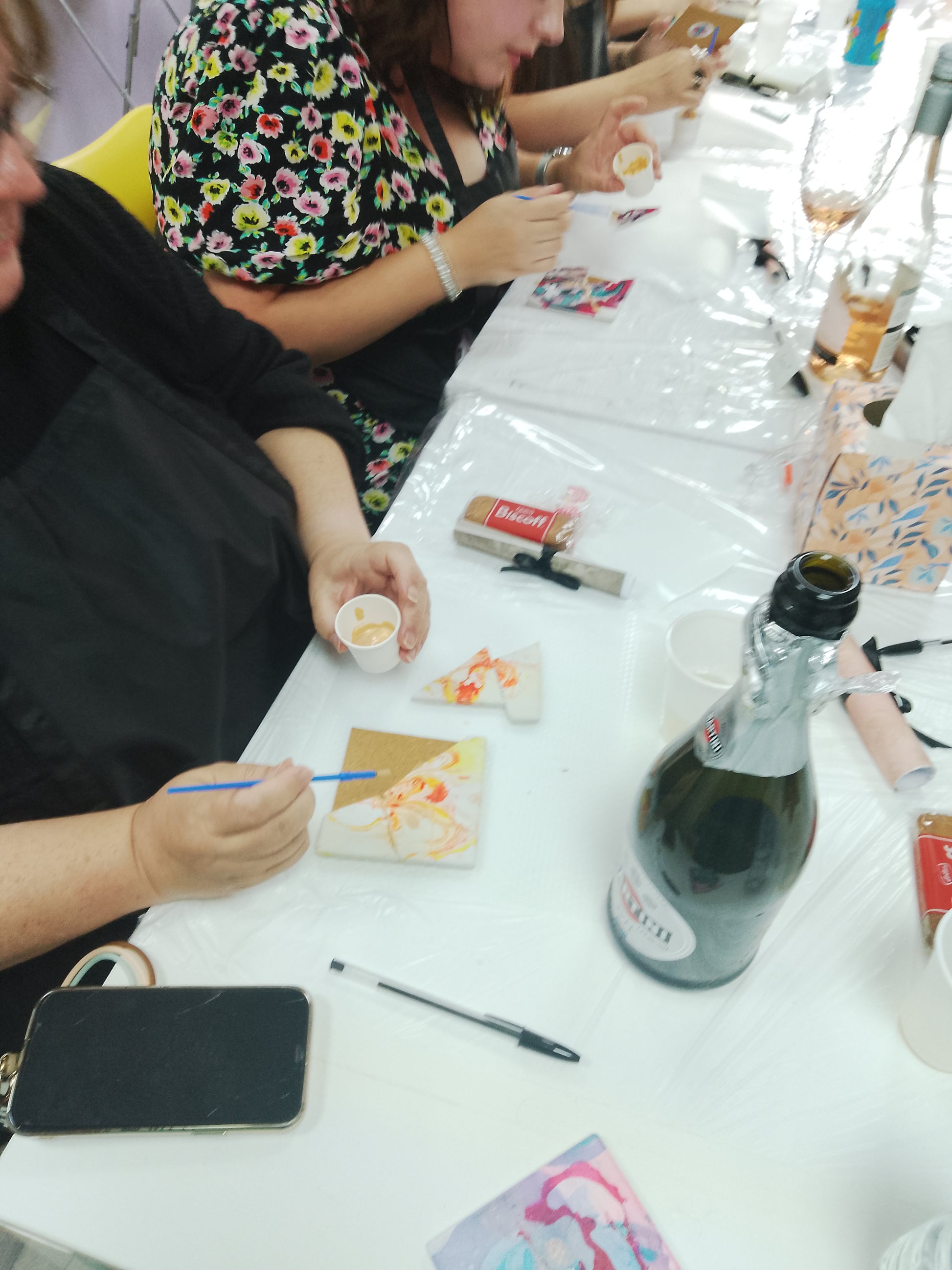 People sitting at a table with art supplies and a bottle of wine.