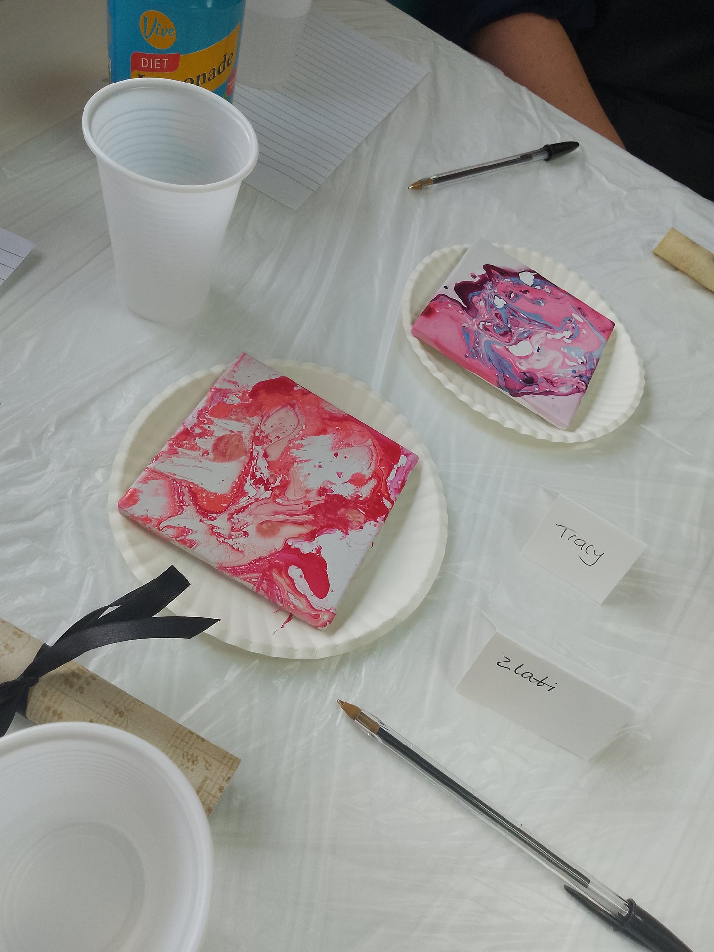 Marbled pink and white coasters on a table with cups and paintbrushes.