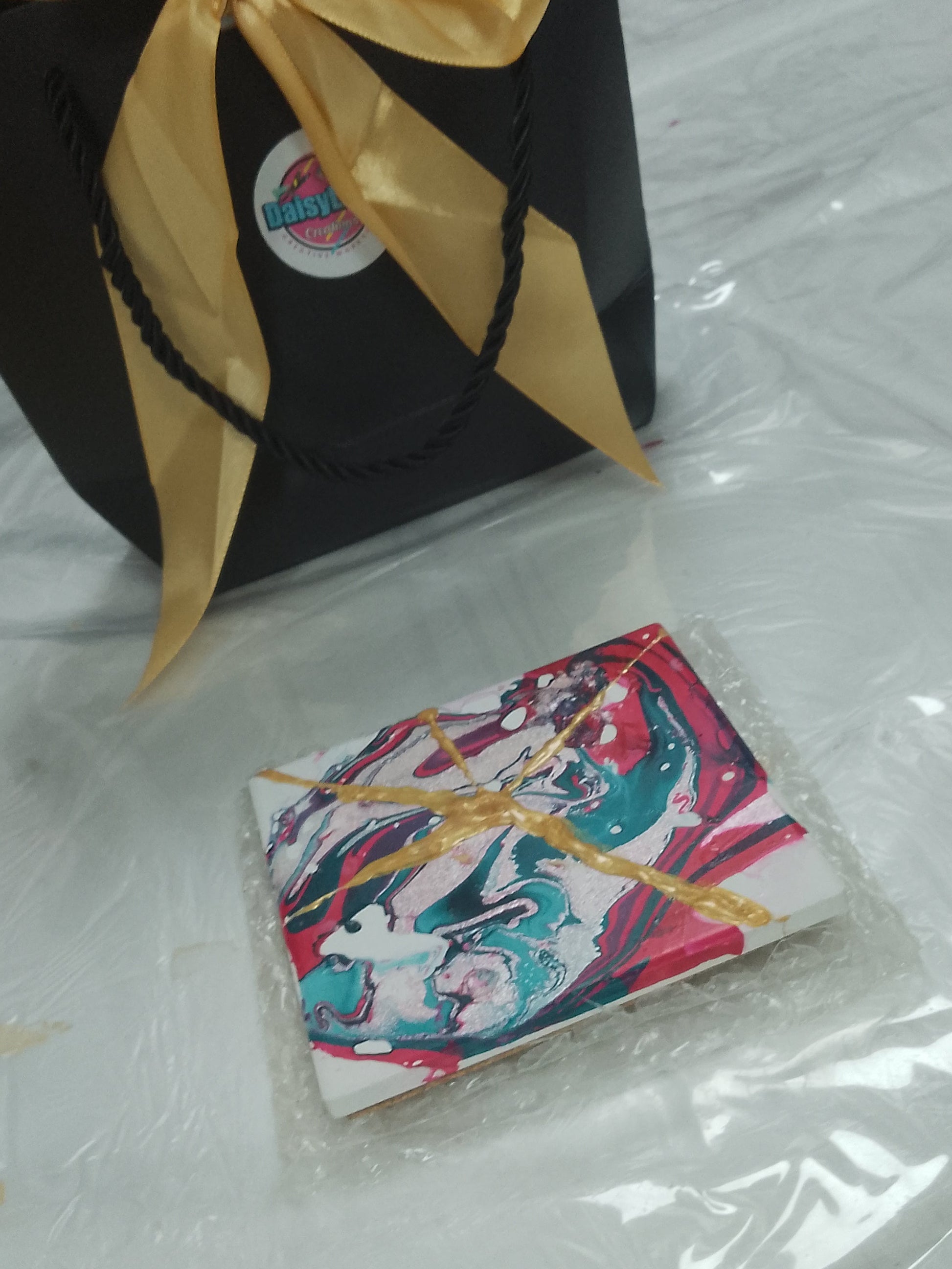 Black gift bag with gold bow and colorful item on a white table.KINTSUGI WORKSHOP MARBLED CERAMIC TILES 